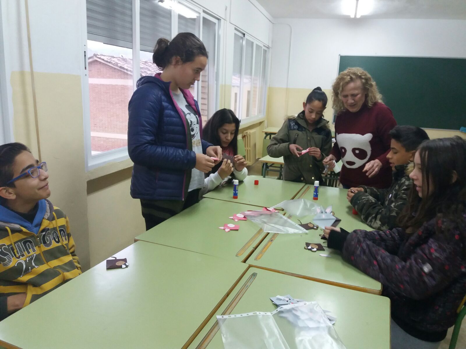 Dos maestras ayudan a niños a realizar manualidades con recortes de papel y pegamento, en un taller de apoyo para familias de pacientes con leucemia mieloide crónica (LMC).