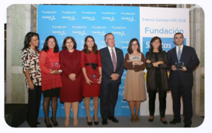 Grupo de ocho personas (6 mujeres y 2 hombres) sonriendo con premios en evento de Fundación Sanitas, fondo azul.