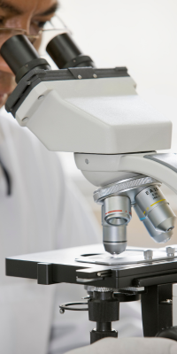 Laboratorista especializado examinando células sanguíneas en microscopio para diagnóstico de leucemia y otros cánceres hematológicos.