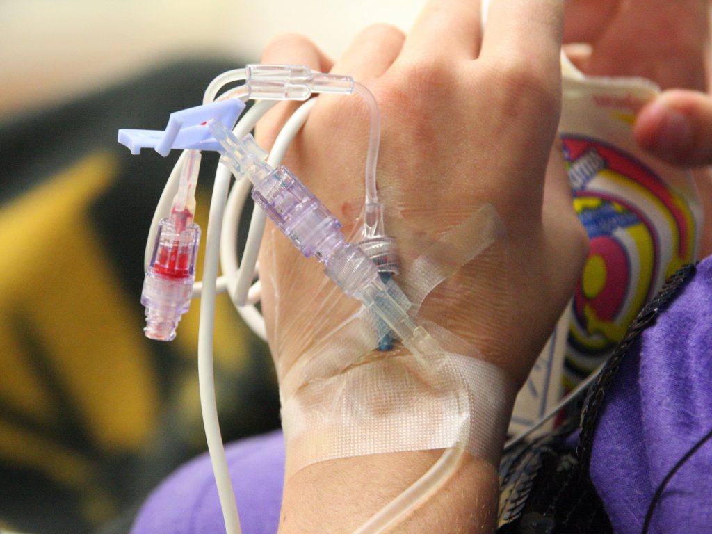 Mano de paciente recibiendo una canalización intravenosa por parte de un profesional de la salud, con aguja y vendaje en vena.